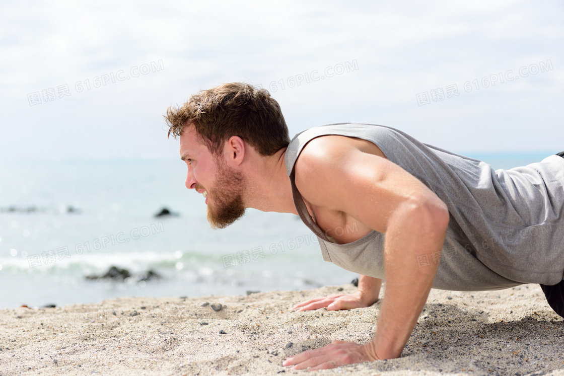 海边沙滩上做俯卧撑的男子高清图片