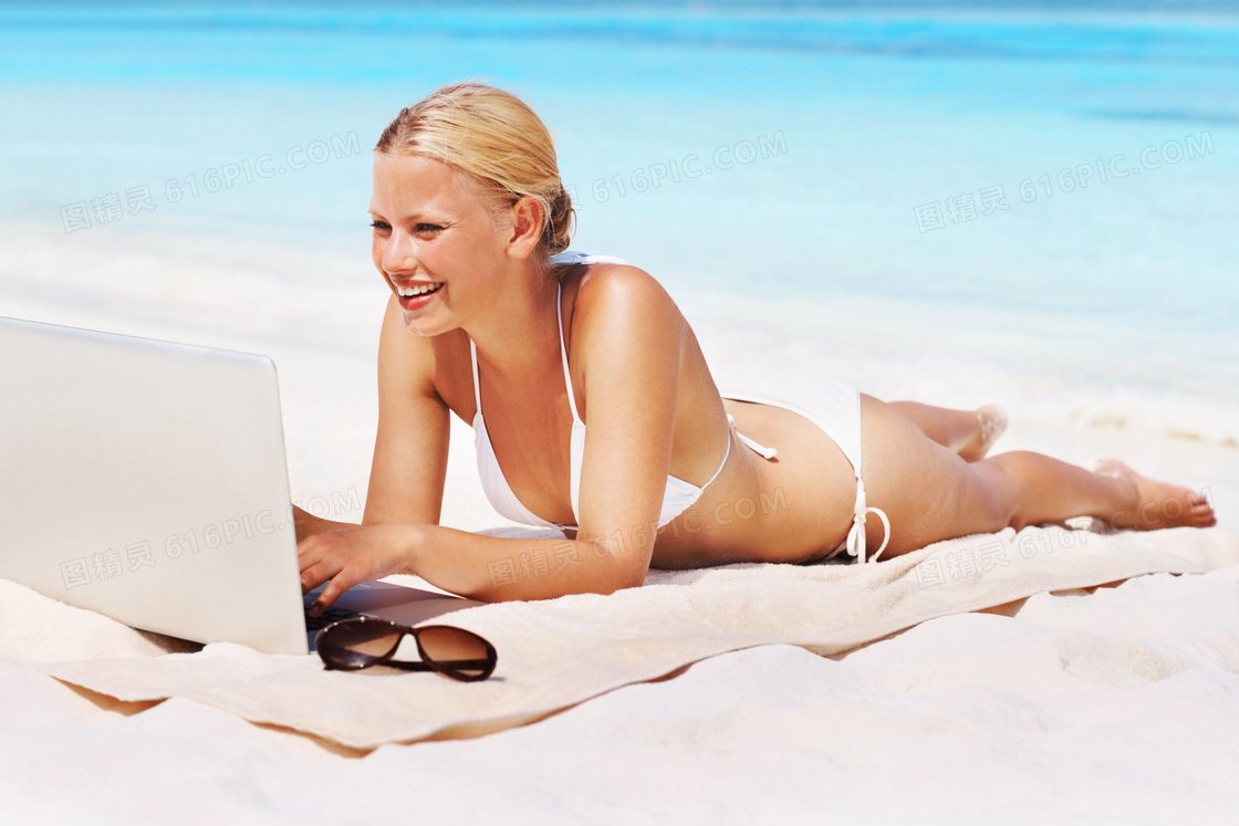沙滩上趴着玩电脑的美女高清摄影图片